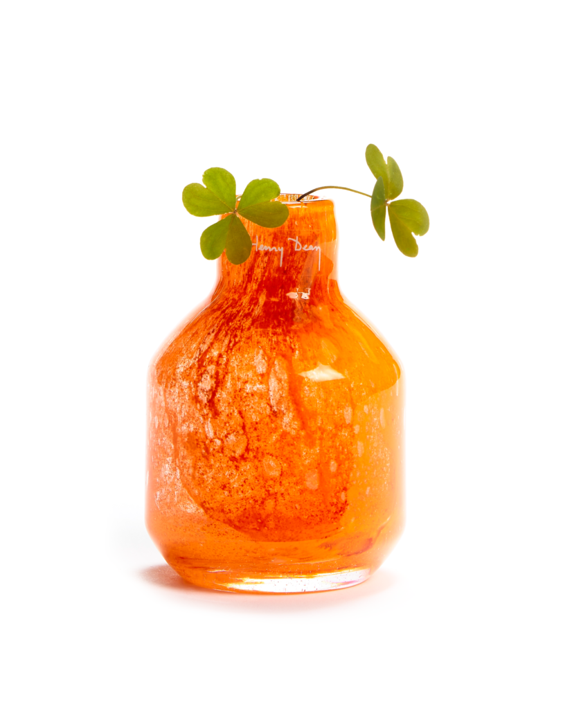 Short bright orange opaque handmade glass object with two clovers