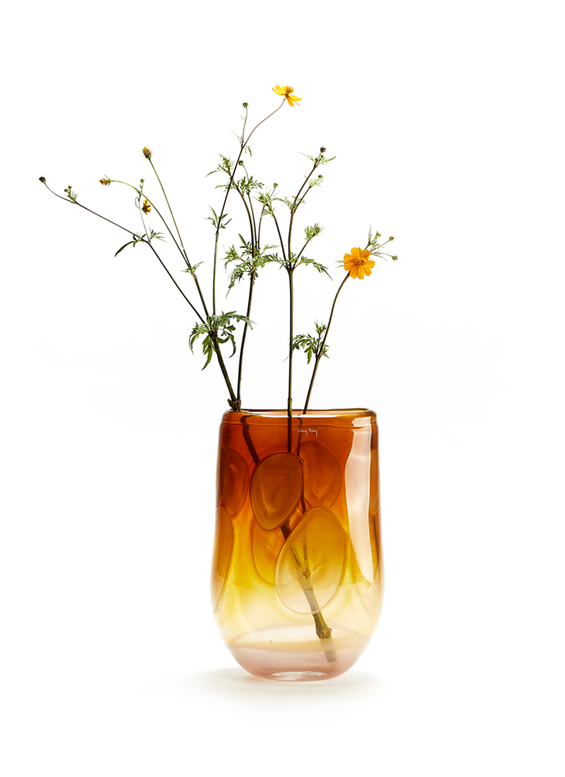 tall handmade glass vase in brown yellow orange color with a brach with flowers